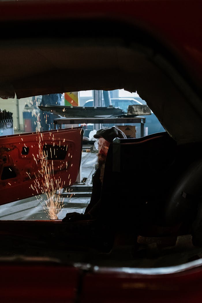 A mechanic performs welding inside a car at a workshop, showcasing sparks and repair work.